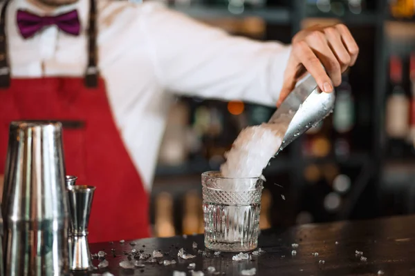 バーカウンターのカクテルグラスに氷を追加白いシャツのバーテンダー — ストック写真