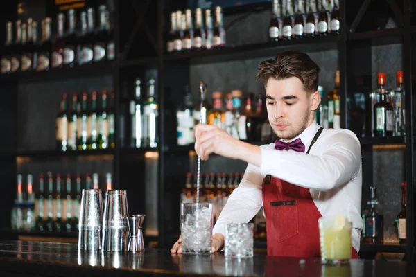 Barman holding a long spoon and glass filled with ice cubes on the bar counter — Stock Photo, Image