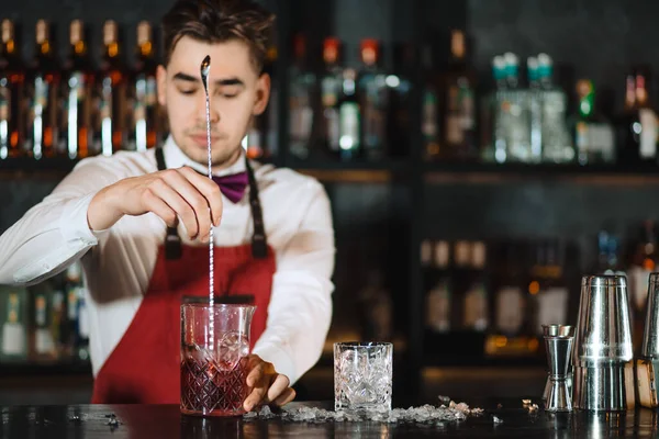 Barman trzyma długą łyżkę i szklankę wypełnioną kostkami lodu na blacie. — Zdjęcie stockowe