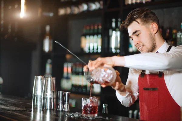Barman tenant une longue cuillère et du verre rempli de glaçons sur le comptoir du bar — Photo