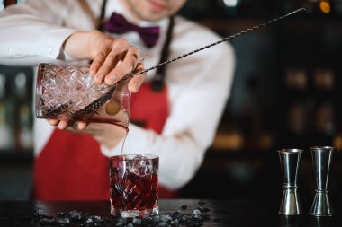 Barmen barın üstündeki bardağa taze kokteyl döküyor.