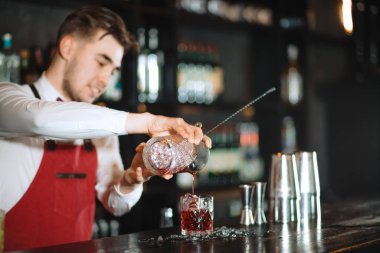Barmen uzun bir kaşık ve bardakla barın üstünde buz küpleri tutuyor.