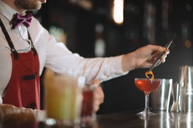 Barmen bar tezgahında cımbızla portakal aromalı kokteyl ekliyor.