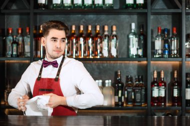 Barda duran barmen, havluyla bardakları temizliyor.