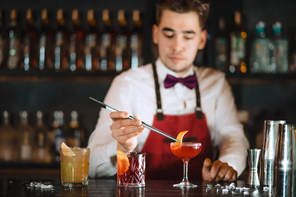 Бармен, який додає до коктейлю апельсиновий жест з щипцями на стійці бару. — стокове фото