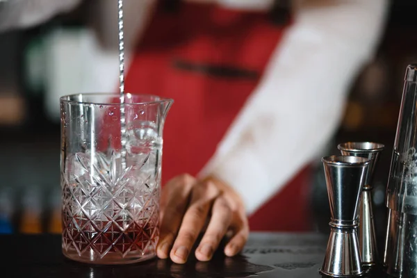 Barman holding a long spoon and glass filled with ice cubes on the bar counter — Stock Photo, Image