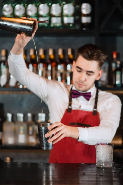 Barman derramando coquetel fresco da coqueteleira no vidro no balcão do bar — Fotografia de Stock