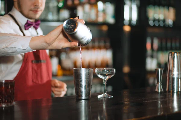 Barmann gießt frischen Cocktail aus dem Shaker ins Glas auf der Theke — Stockfoto