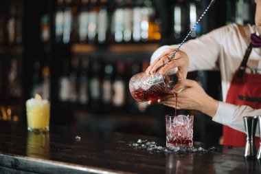 Barmen barın üstündeki bardağa taze kokteyl döküyor.