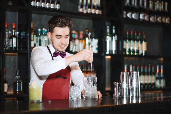 Barman sosteniendo una cuchara larga y un vaso lleno de cubitos de hielo en el mostrador de la barra —  Fotos de Stock