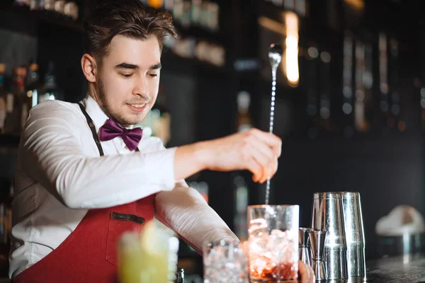 Barman tiene un cucchiaio lungo e un bicchiere pieno di cubetti di ghiaccio sul bancone del bar — Foto Stock