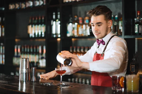 Barman wlewa świeży koktajl z shakera do szklanki na blacie. — Zdjęcie stockowe