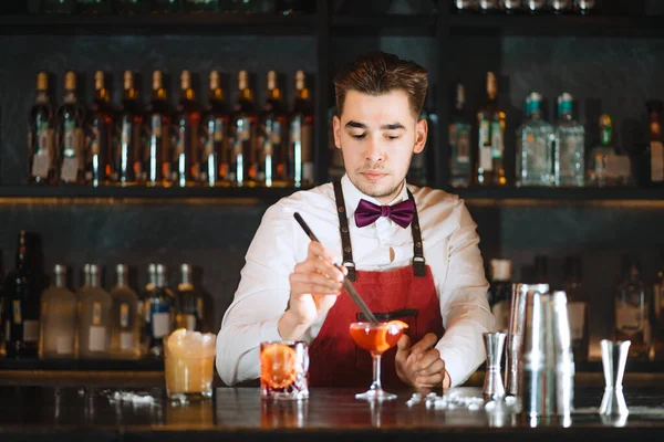 Barmen bar tezgahında cımbızla portakal aromalı kokteyl ekliyor. — Stok fotoğraf