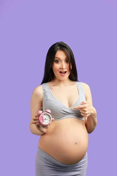 Foto de primer plano de la mujer embarazada en ropa interior que sostiene el despertador rojo en la barriga — Foto de Stock