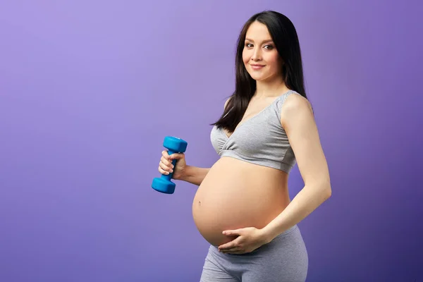 Feliz mamá embarazada haciendo ejercicio en el estudio con pesas sobre fondo violeta — Foto de Stock