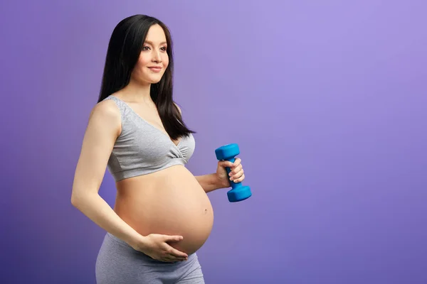 Feliz mamá embarazada haciendo ejercicio en el estudio con pesas sobre fondo violeta — Foto de Stock