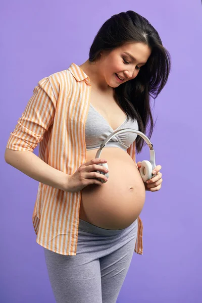 Hamile kadın, bebeğinin doğanın seslerini duyması için kulaklığı karnına dayıyor. — Stok fotoğraf