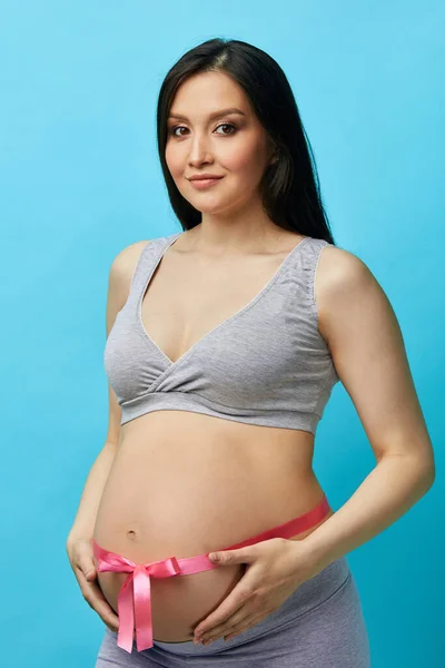 Imagen recortada de una hermosa mujer embarazada abrazando su barriga con cinta rosa —  Fotos de Stock