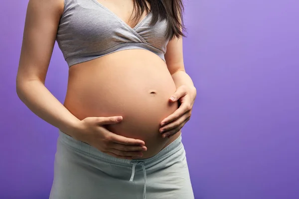 Iubind femeie însărcinată ținându-și burta în timp ce pozează în studio — Fotografie, imagine de stoc
