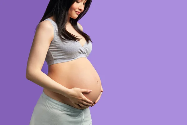 Iubind femeie însărcinată ținându-și burta în timp ce pozează în studio — Fotografie, imagine de stoc