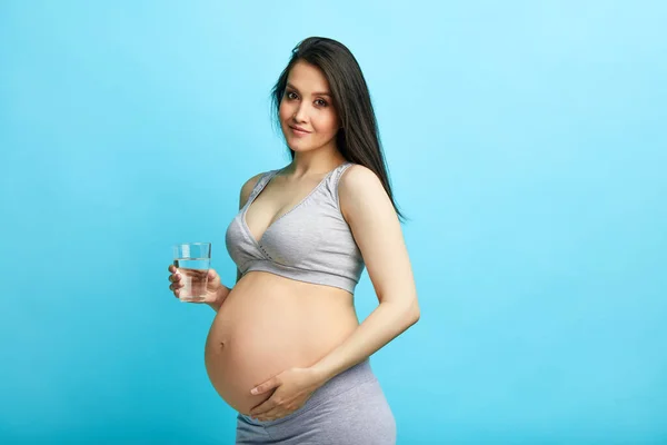 Молода вагітна біла модель з довгим чорним волоссям, що тримає склянку води . — стокове фото