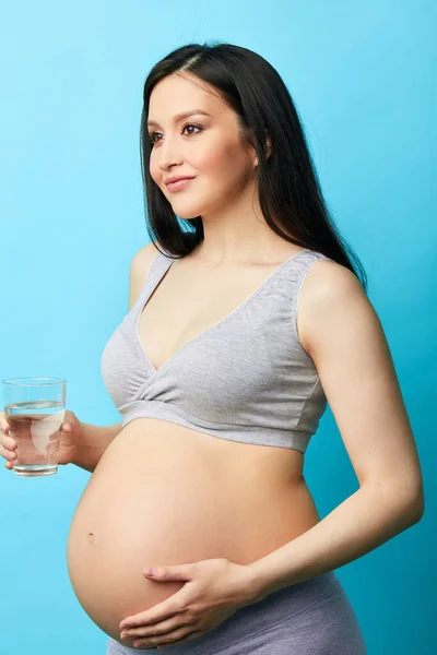 Joven modelo caucásico embarazada con pelo largo negro sosteniendo un vaso de agua . — Foto de Stock