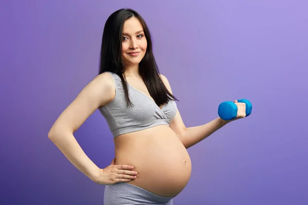 Feliz mamá embarazada haciendo ejercicio en el estudio con pesas sobre fondo violeta — Foto de Stock