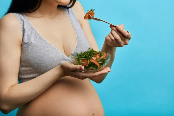 Ізольований знімок майбутньої молодої матері, що їсть здорову їжу на синьому фоні — стокове фото