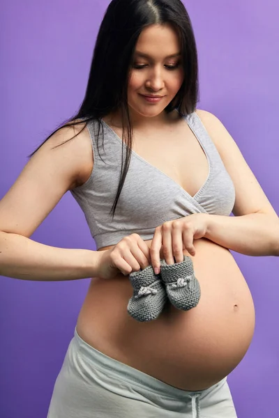 Chaussons bébé pour enfant à naître sur le ventre de la femme enceinte posant à l'intérieur — Photo