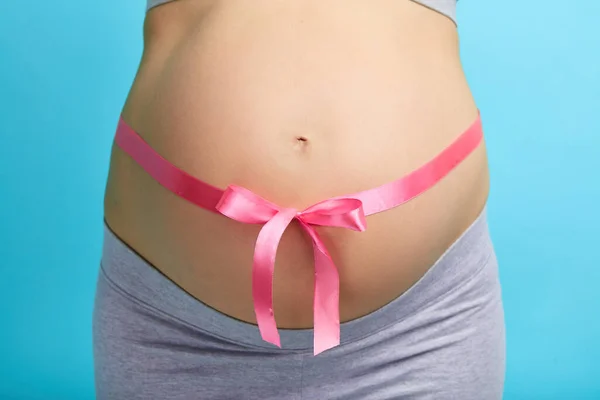 Όμορφη έγκυος γυναίκα δένει την κοιλιά της με ροζ κορδέλα — Φωτογραφία Αρχείου