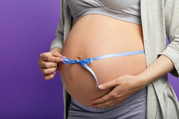 Vágott kép gyönyörű terhes nő átöleli a pocakját kék szalaggal — Stock Fotó
