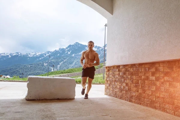 Jovem atleta homem em shorts esportivos correndo enquanto se exercita fora — Fotografia de Stock
