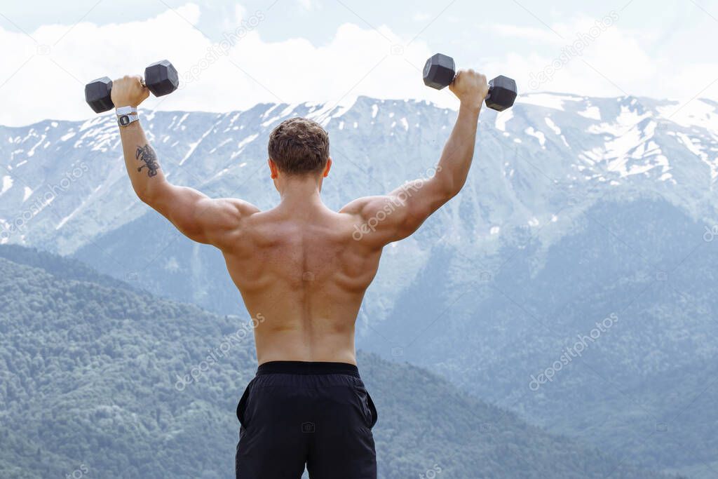 Muscular male athlete with arms raised doing lifting exercises dumbbells.