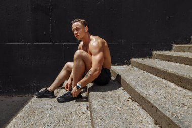 Yakışıklı, beyaz tenli sporcu merdivenlerde oturuyor ve bağcıklarını bağlıyor.