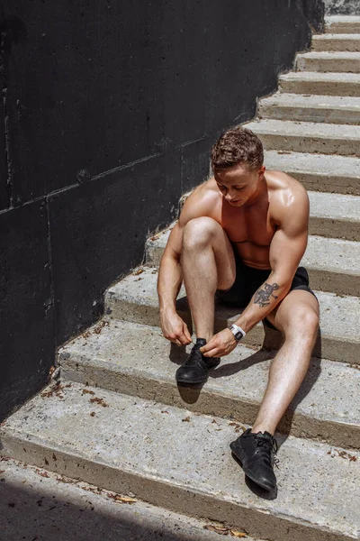 Guapo joven atleta caucásico sentado y atando cordones en las escaleras —  Fotos de Stock
