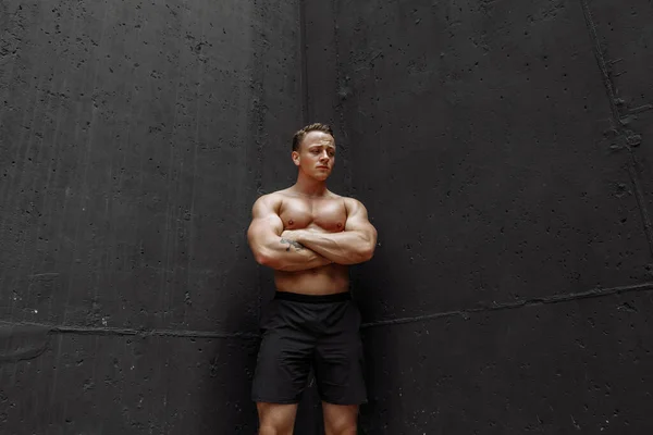 Strong and muscular bodybuilder showing his body near concrete wall — Stock Photo, Image