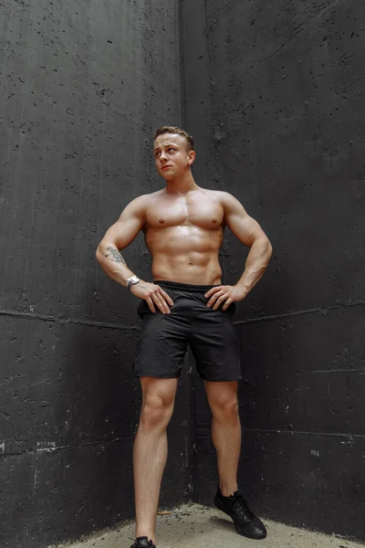 Forte e musculoso fisiculturista mostrando seu corpo perto de parede de concreto — Fotografia de Stock