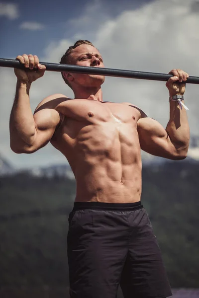 Sport man gör pull-up övning på en horisontell bar mot en blå himmel. — Stockfoto