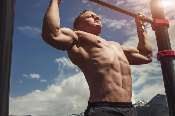 Homem de esportes fazendo exercício pull-up em uma barra horizontal contra um céu azul . — Fotografia de Stock