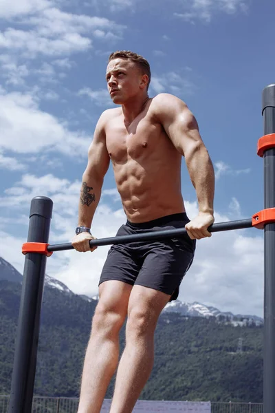 Homem de esportes fazendo exercício pull-up em uma barra horizontal contra um céu azul . — Fotografia de Stock