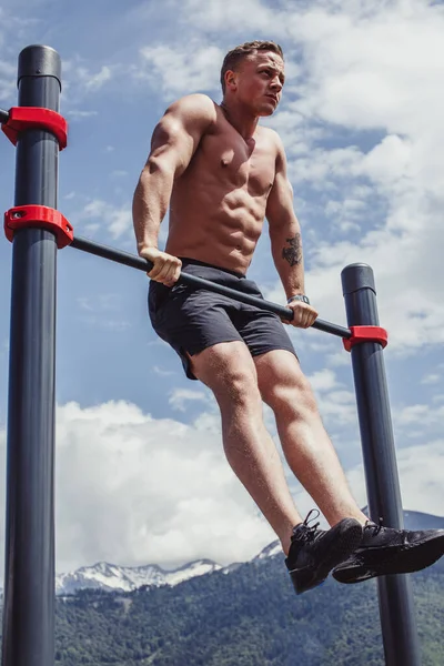 Sport man gör pull-up övning på en horisontell bar mot en blå himmel. — Stockfoto