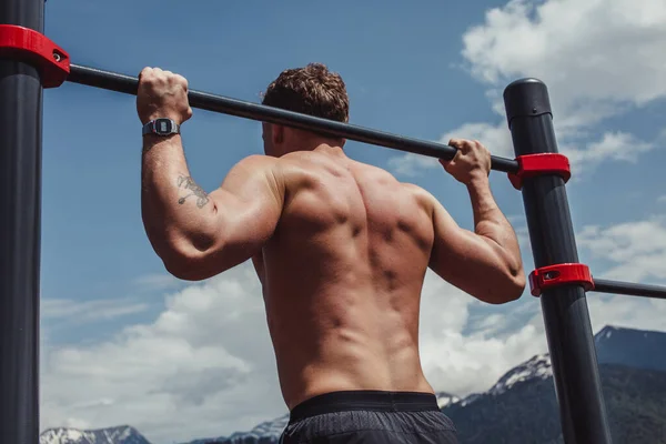 Sport man gör pull-up övning på en horisontell bar mot en blå himmel. — Stockfoto