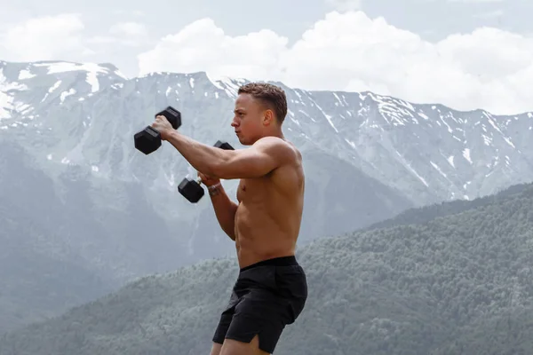 Muskulös manlig idrottsman med upphöjda armar som tränar hantlar. — Stockfoto