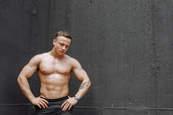 Modelo de fitness hombre de pie sobre fondo gris, una pierna doblada contra la pared, mirando hacia abajo, espacio de copia — Foto de Stock