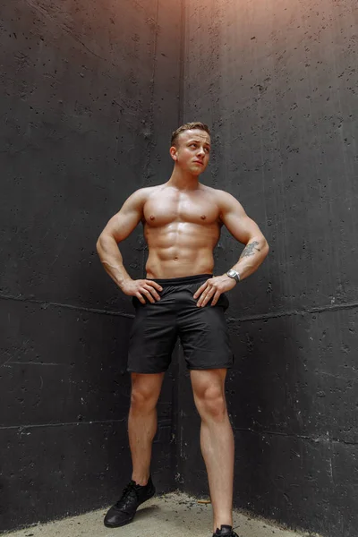 Fitness model muž stojící na šedém pozadí, jednu nohu ohnutou ke zdi, pohled dolů, kopírovací prostor — Stock fotografie