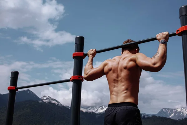 Sports man doing pull-up exercise on a horizontal bar against a blue sky. — Stock Photo, Image