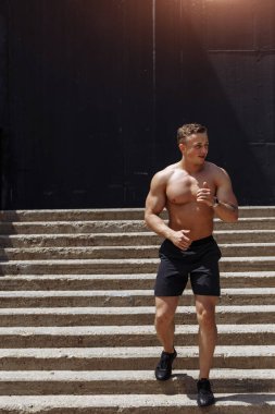 Beyaz tişörtsüz atletik koşucu şehirde merdivenlerden inip çıkıyor.