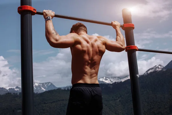 Spor adamı mavi gökyüzüne karşı yatay bir çubukta barfiks egzersizi yapıyor.. — Stok fotoğraf