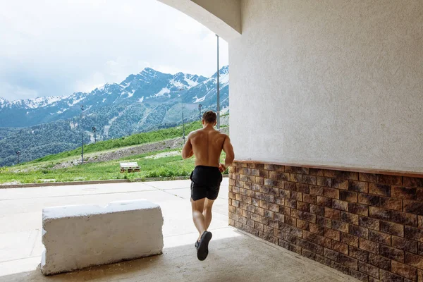 Jovem atleta homem em shorts esportivos correndo enquanto se exercita fora — Fotografia de Stock