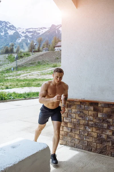 Jovem atleta homem em shorts esportivos correndo enquanto se exercita fora — Fotografia de Stock